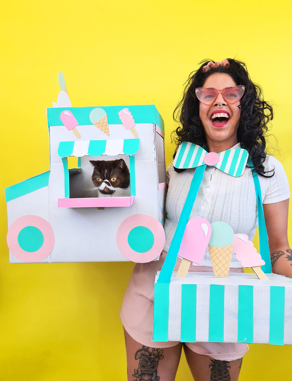 On a yellow background sits a pink, white and green painted 'boxtume' of an icecream truck created by Kitiya Palaskas