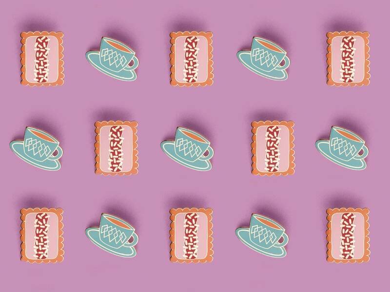 A collection of afternoon-tea enamel pins laid out in a diagonal grid formation on a purple background. One pin design is a cup of tea and one is a biscuit.
