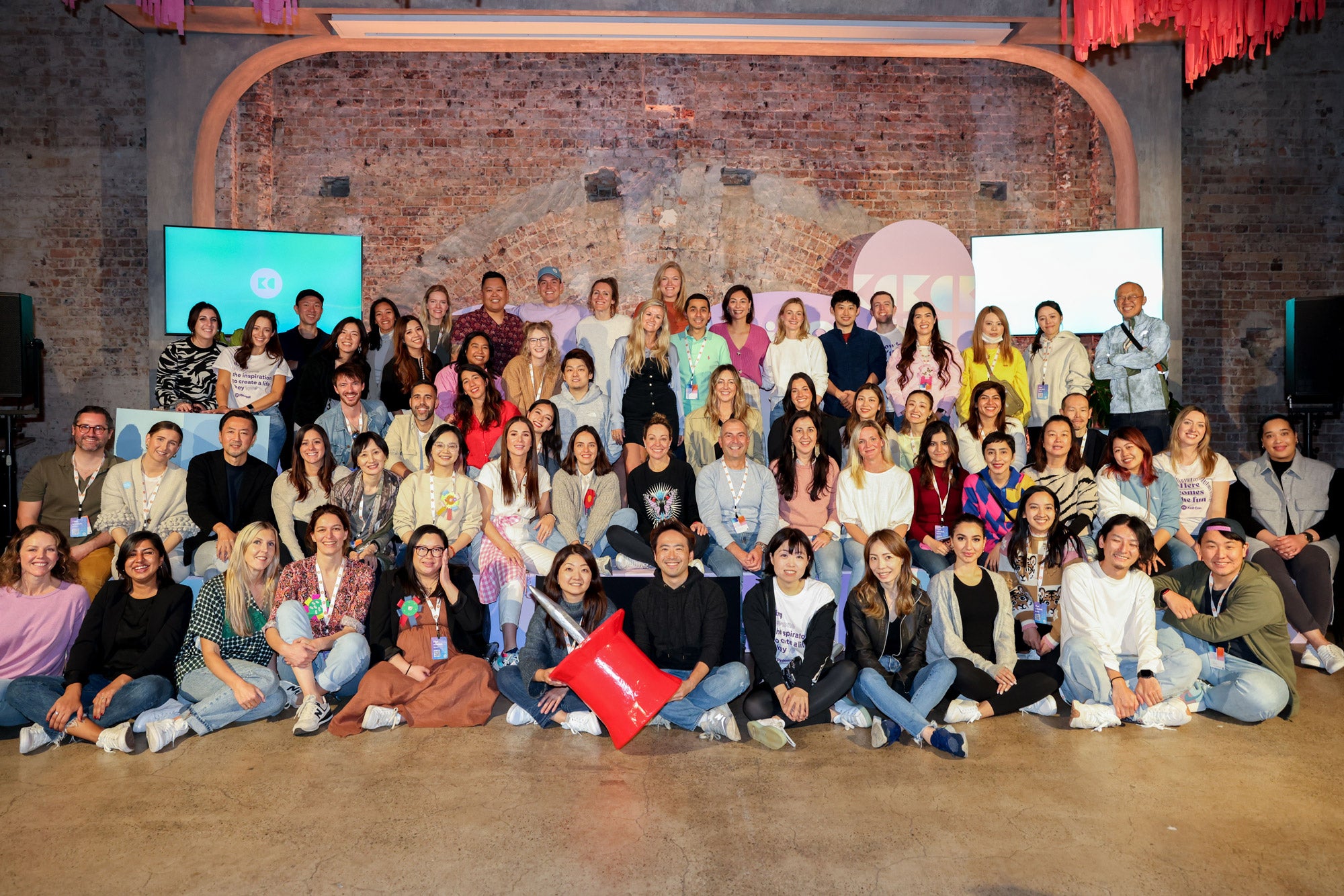 A group of people pose in an auditorium with a giant papier-mâché pin prop. 