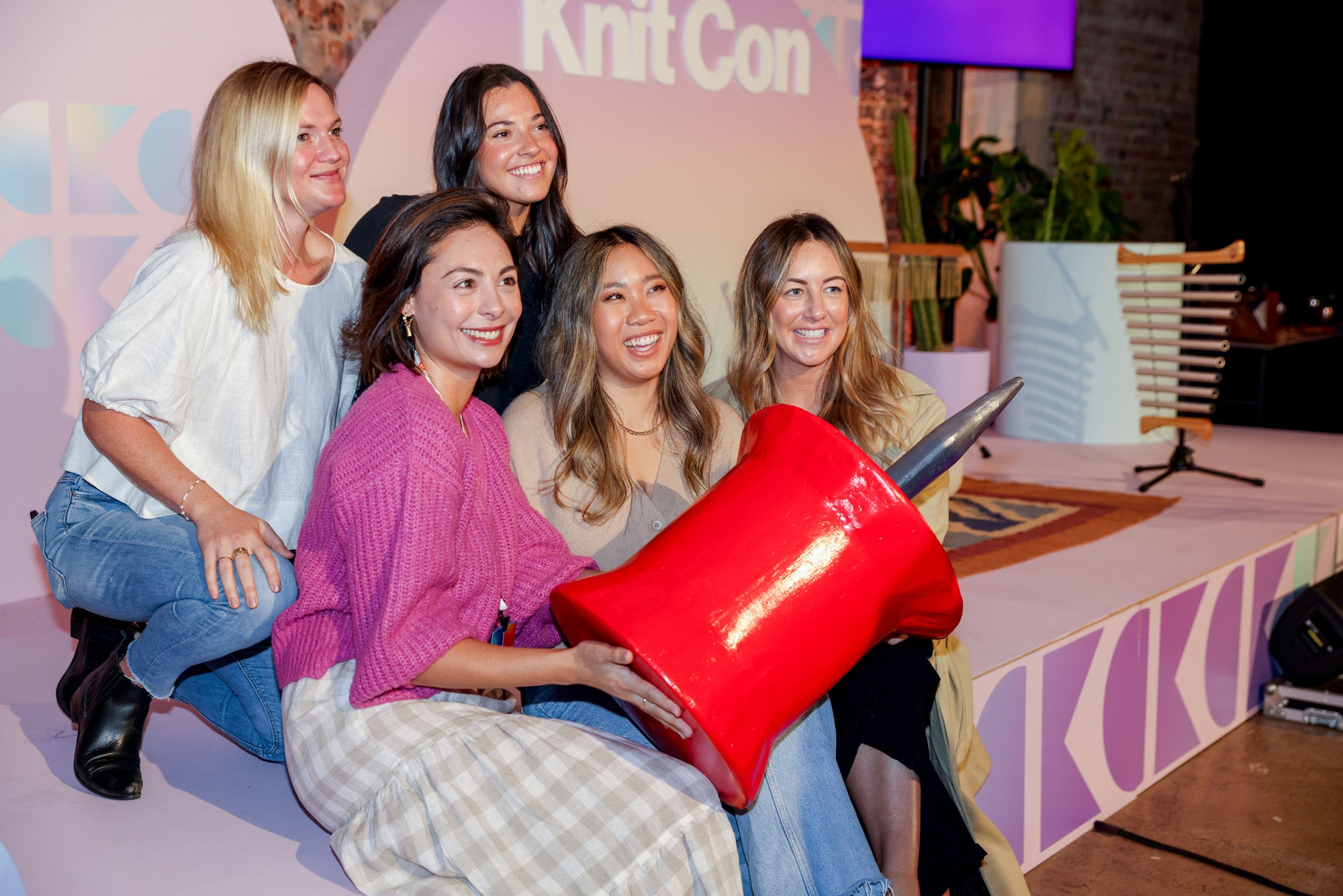 A group of people pose in an auditorium with a giant papier-mâché pin prop. 