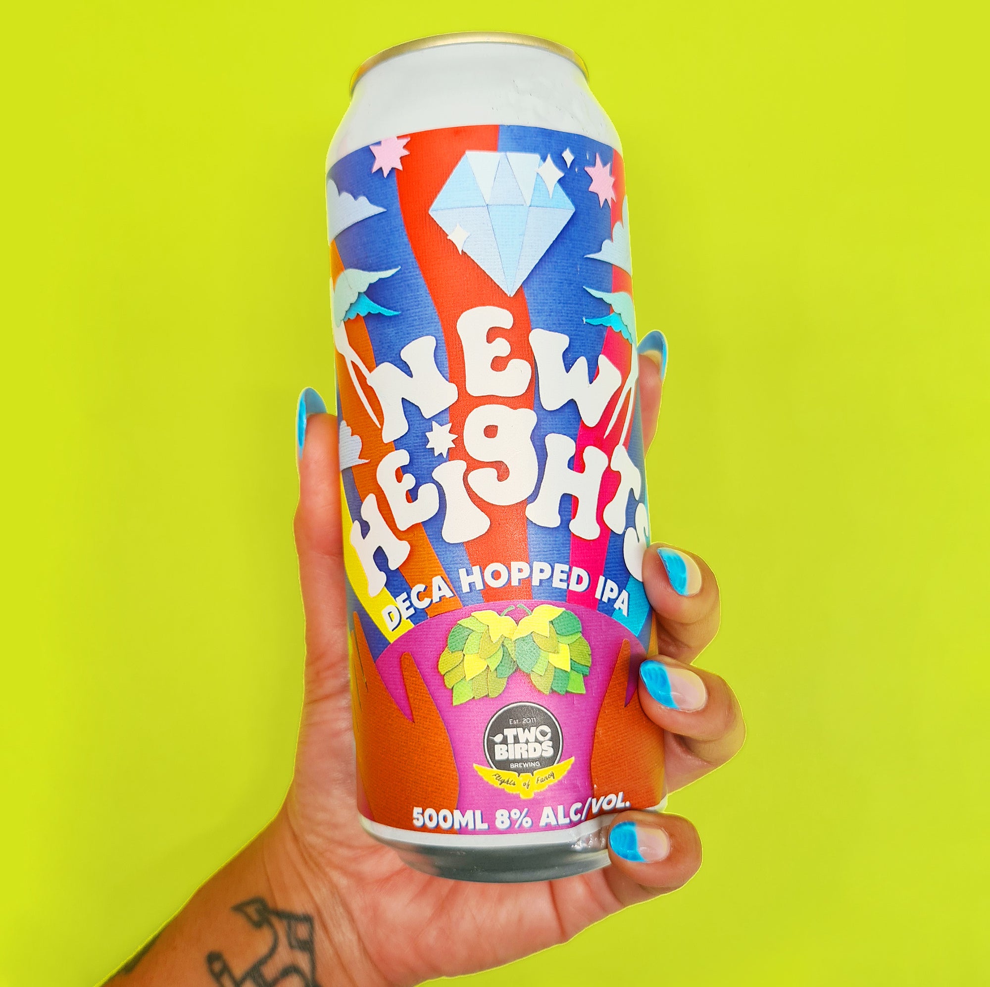 A brown hand with long decorated nails holds a colourful beer can with papercraft collage illustrated label.